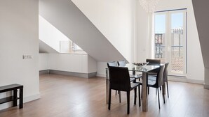 Un área de comedor moderna con una mesa y sillas de vidrio, una lámpara colgante y vistas de la ciudad a través de un ventanal grande.