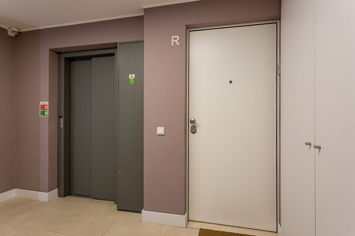Area ascensore con porta dell'ascensore chiusa, segnale di allarme antincendio e una porta contrassegnata con la lettera 'R'.