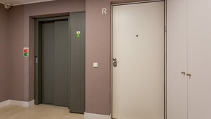 Zona de ascensores con puerta de ascensor cerrada, señal de alarma contra incendios y una puerta con la letra 'R'.