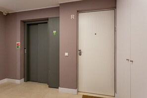 Ein Aufzugsbereich mit einer geschlossenen Aufzugtür, einem Feuerschutzschild und einer Tür mit dem Buchstaben 'R'.
