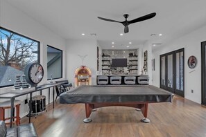 A modern living room with a pool table, a large window, and a ceiling fan. - The Very Best Tulsa has to offer! (Tulsa)