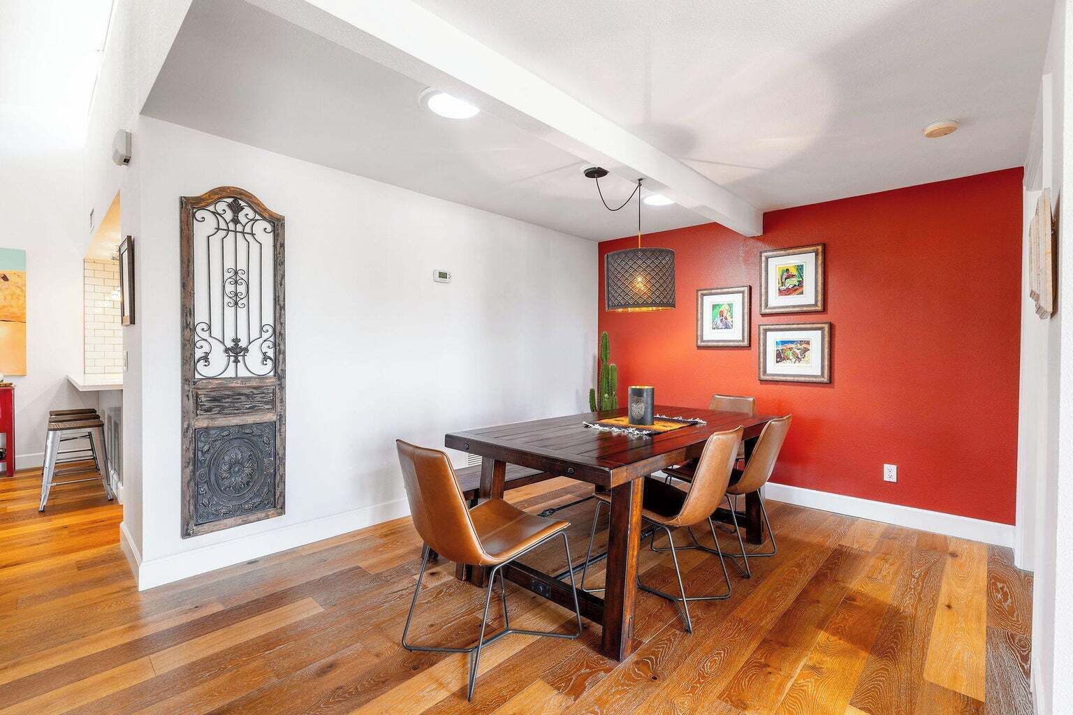 Un coin repas avec une table et des chaises en bois, un mur d’accent rouge et un portail décoratif en métal.
