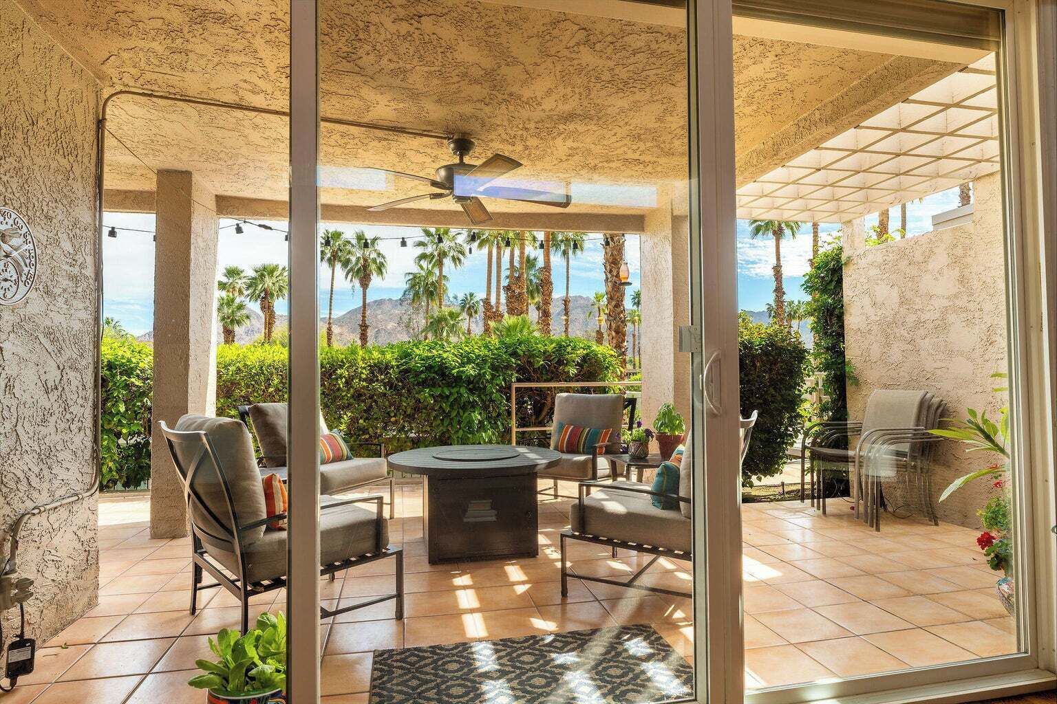 A covered outdoor seating area with chairs and a table, overlooking a scenic view with palm trees and mountains.