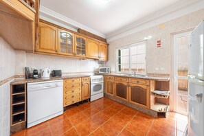 A kitchen with wooden cabinets, a white dishwasher, a stove, a microwave, and a window. - GuestReady - Superb house w/ garden & patio (Almada)