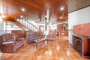 A spacious living area with a high ceiling, leather sofas, a dining table, and a fireplace. - GuestReady - Superb house w/ garden & patio (Almada)