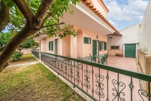 A building with a balcony, green shutters, and a paved area with a metal railing. - GuestReady - Superb house w/ garden & patio (Almada)