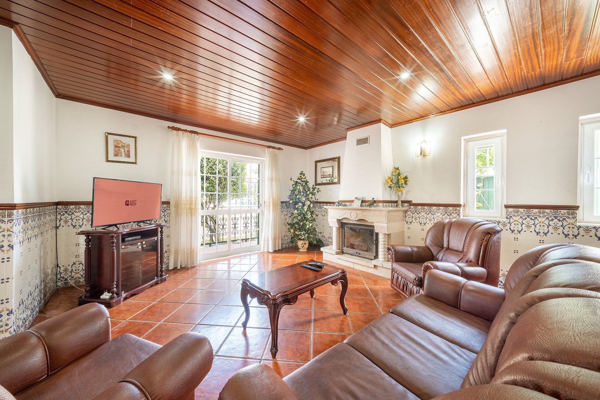 A living room with leather sofas, a fireplace, a television, and a large window with a view of greenery.