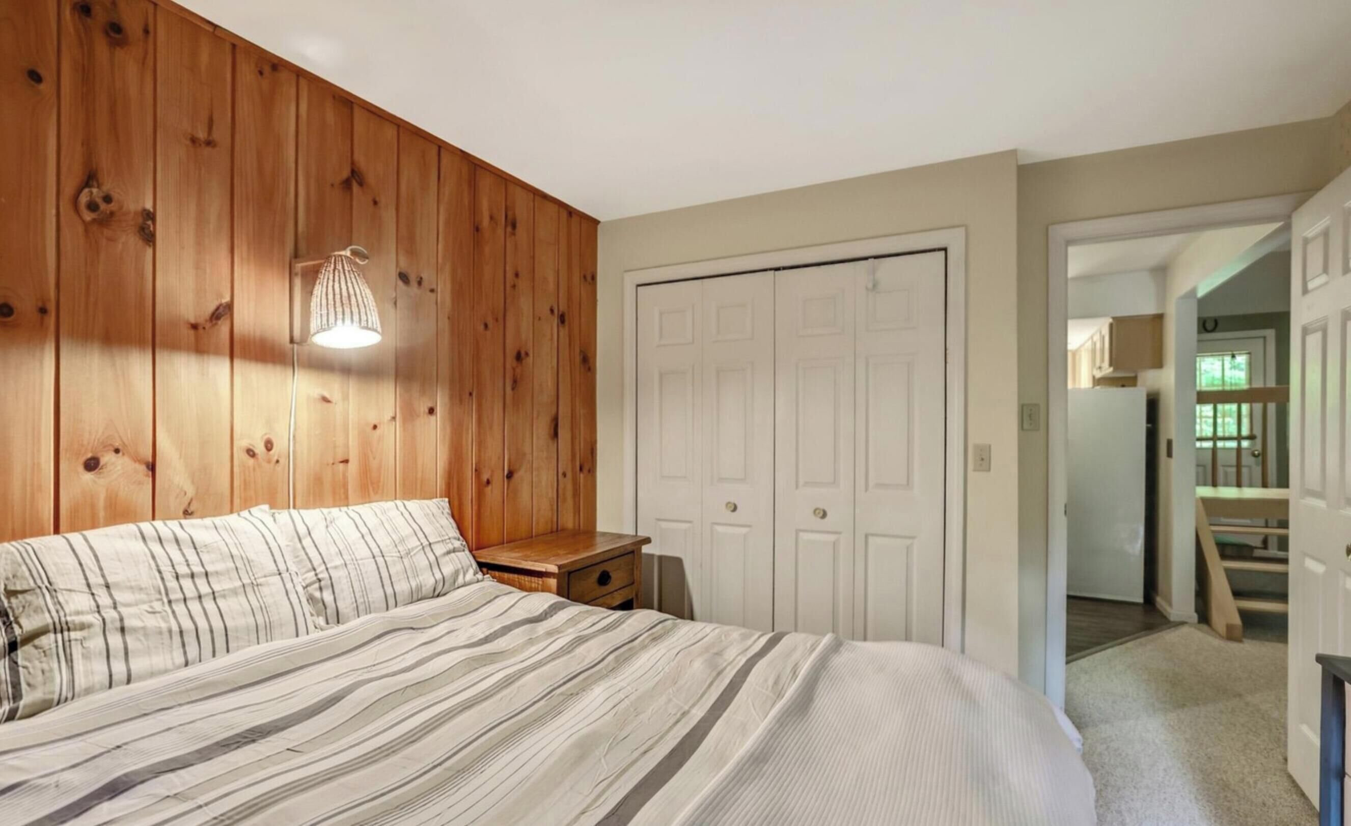Ein Schlafzimmer mit einem Holzkopfteil, einem Bett mit gestreifter Bettwäsche, einem Nachttisch und einer weißen Tür.