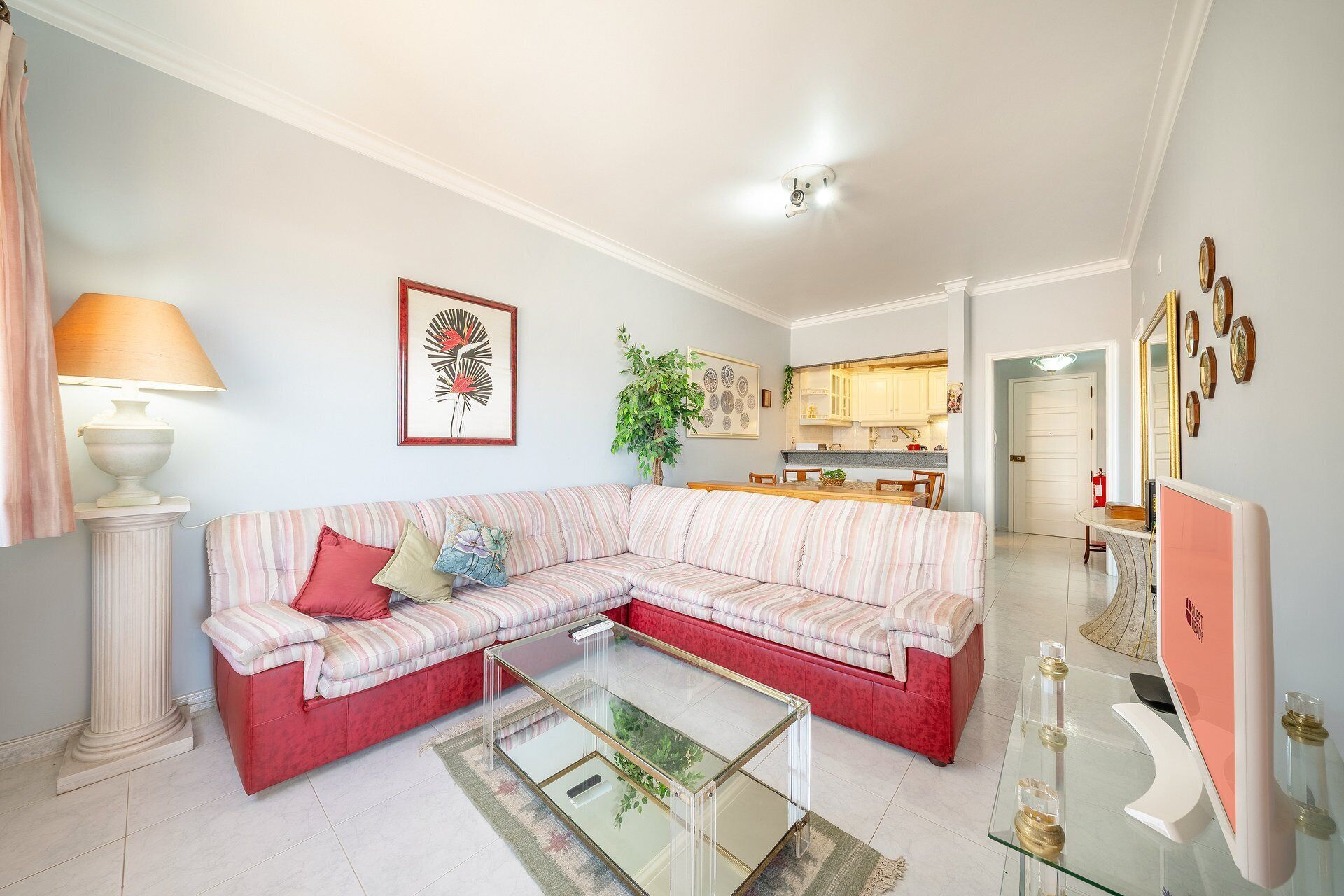 A living room with a sectional sofa, a glass coffee table, and a kitchen in the background.