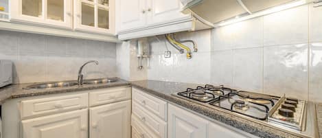 A kitchen with white cabinetry, a stainless steel sink, a gas stove, and a range hood.