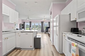 A modern kitchen with white cabinetry, a central island, and a view to the outdoors. - King Bed 1BR Condo | Golf View | Pool (Myrtle Beach)