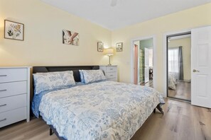 A bedroom with a bed, bedside tables, a lamp, and a door leading to another room. - King Bed 1BR Condo | Golf View | Pool (Myrtle Beach)