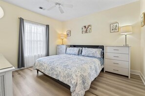 A bedroom with a bed, a nightstand, a lamp, a ceiling fan, and a window with curtains. - King Bed 1BR Condo | Golf View | Pool (Myrtle Beach)
