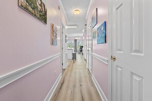 A hallway with a light-colored wooden floor, white doors, and artwork on the walls. - King Bed 1BR Condo | Golf View | Pool (Myrtle Beach)