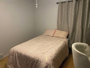 A single bed with a patterned bedspread, a bedside chair, and a wall-mounted light fixture. - 3-bedroom house close to EAA with AC and large FENCED back yard. (Oshkosh)