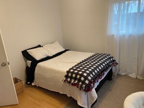 Ein Schlafzimmer mit einem Bett, einer karierten Tagesdecke, einer Tür und einem Fenster mit Vorhängen.
