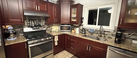 A kitchen with a gas stove, microwave, stainless steel appliances, and wooden cabinets.