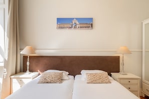 A hotel room with a large bed, two bedside tables with lamps, a wall-mounted picture, and a window with curtains. - GuestReady - Family home near Santa Justa Lift (Lisbon)