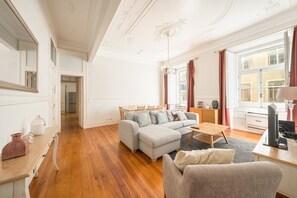 A spacious living room with a large grey sectional sofa, a wooden dining table, and a television on a stand. - GuestReady - Family home near Santa Justa Lift (Lisbon)