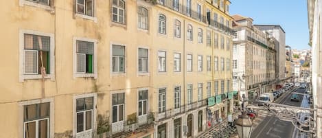 Un immeuble à plusieurs étages doté de balcons, une rue bordée de voitures garées et un ciel dégagé.