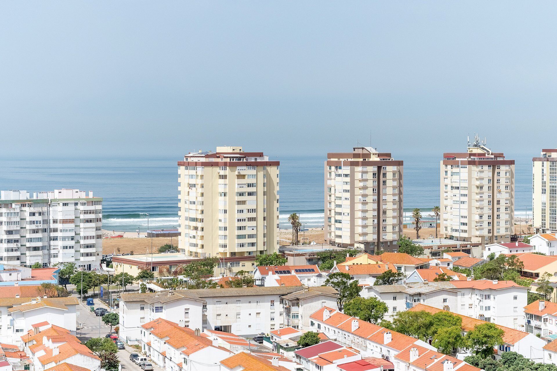 Un quartier résidentiel situé sur la côte, avec des immeubles à plusieurs étages, une plage en arrière-plan et un ciel dégagé.
