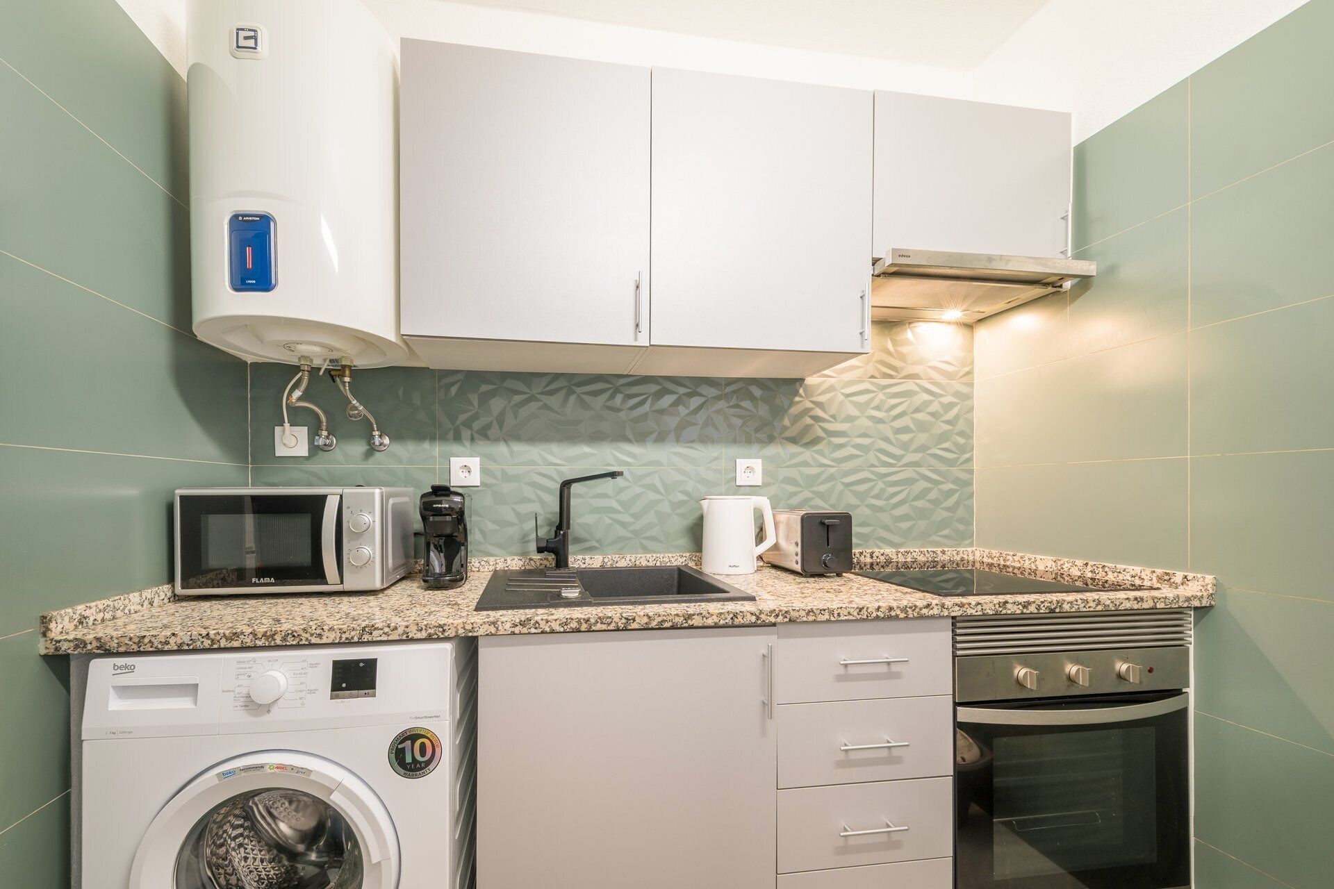 A compact kitchenette with a microwave, coffee maker, toaster, and a washing machine.