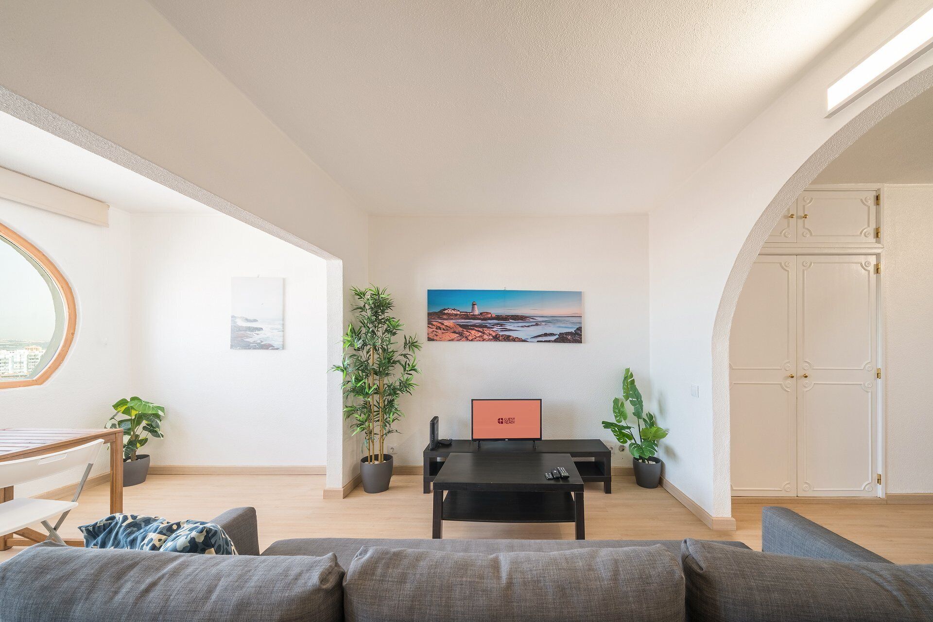 Een woonkamer met een bank, een salontafel, een televisie en een schilderij van een vuurtoren aan de muur.