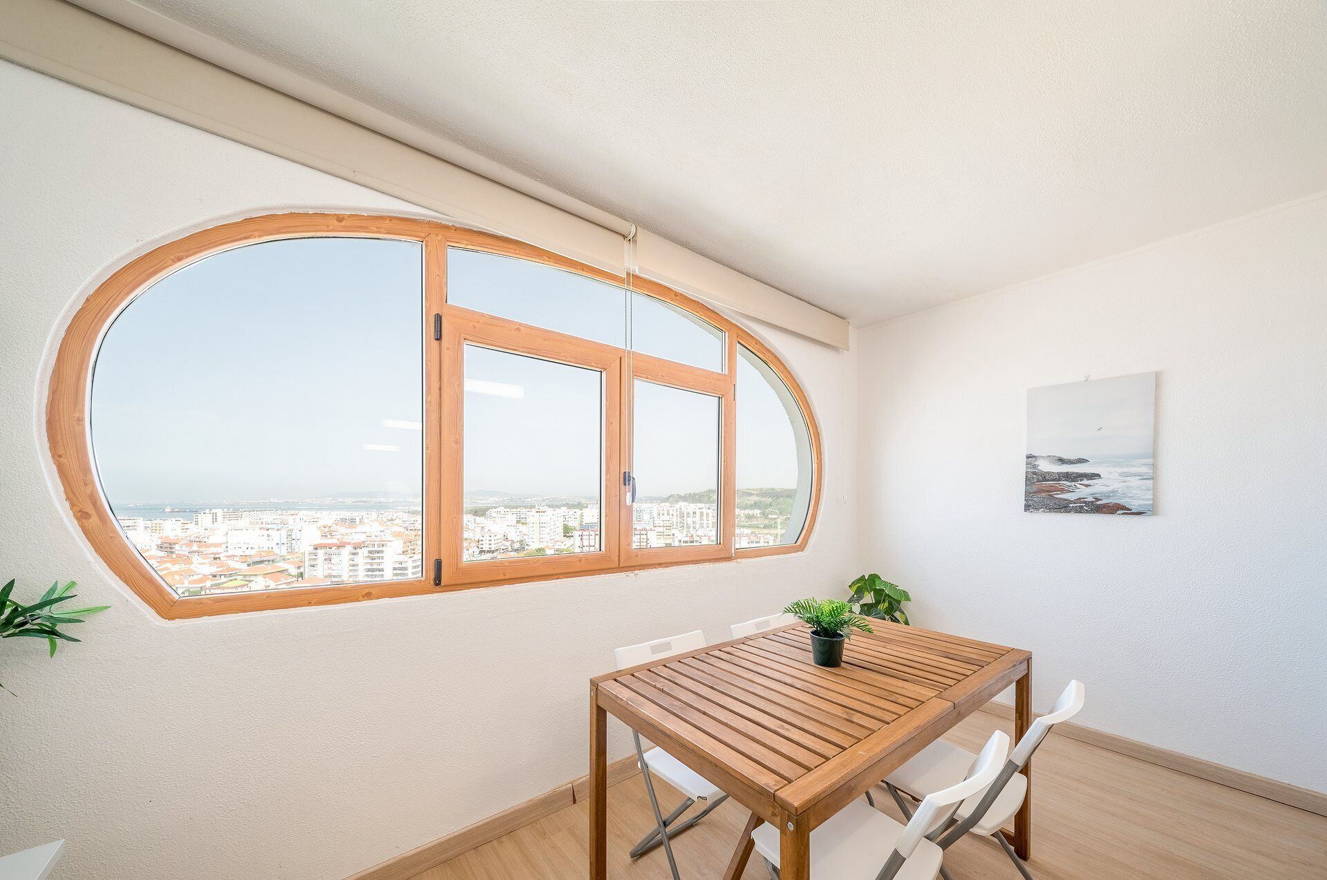 Een kamer met een groot boogvenster, een houten tafel, witte stoelen en een potplant.