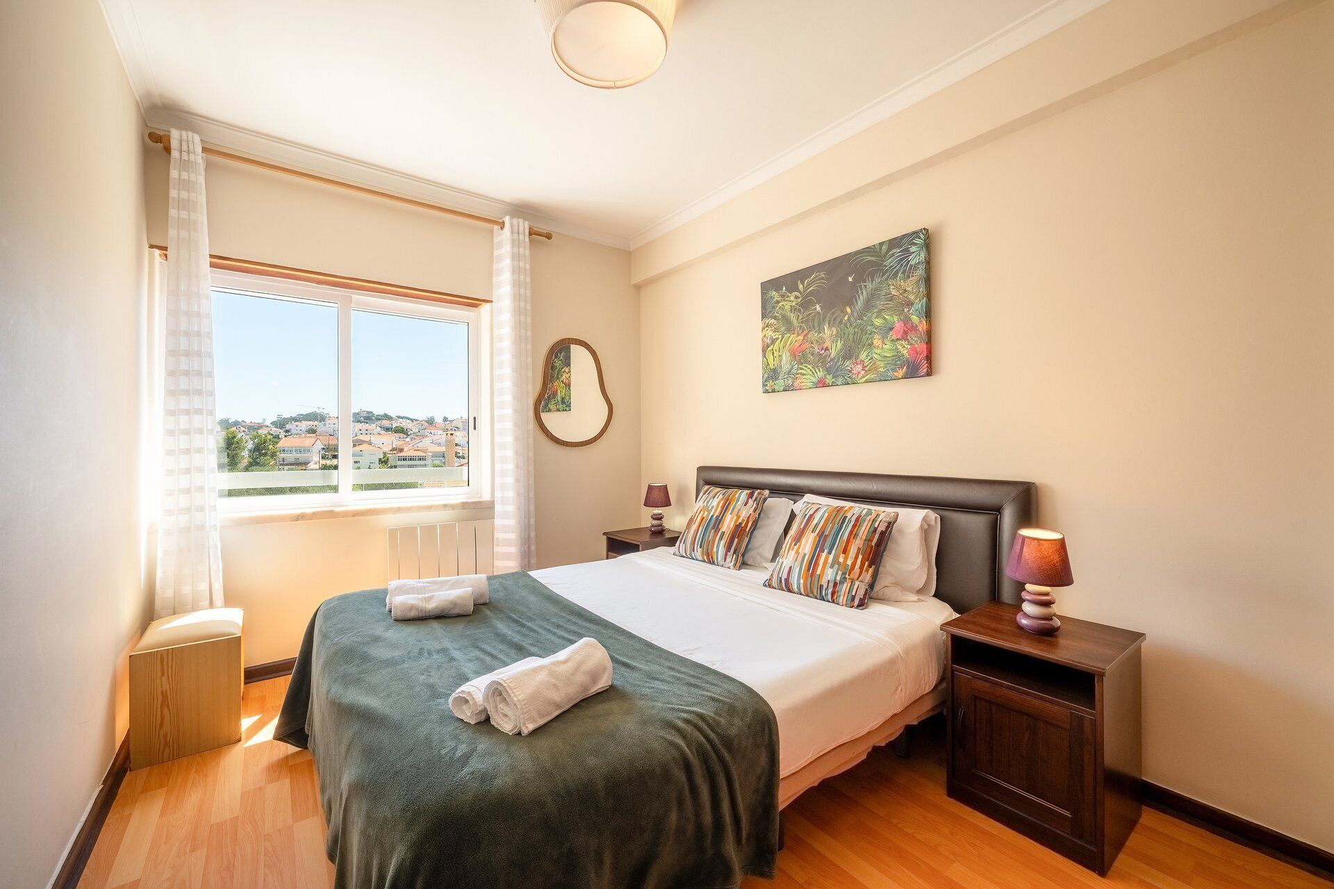 Een hotelkamer met een groot bed, uitzicht op de stad door het raam en een schilderij aan de muur.