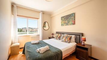 Een hotelkamer met een groot bed, uitzicht op de stad door het raam en een schilderij aan de muur.