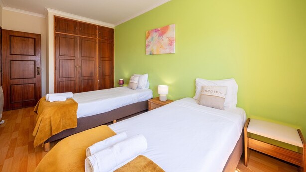 Habitación de hotel con dos camas, un armario de madera, una pared verde y un cuadro.