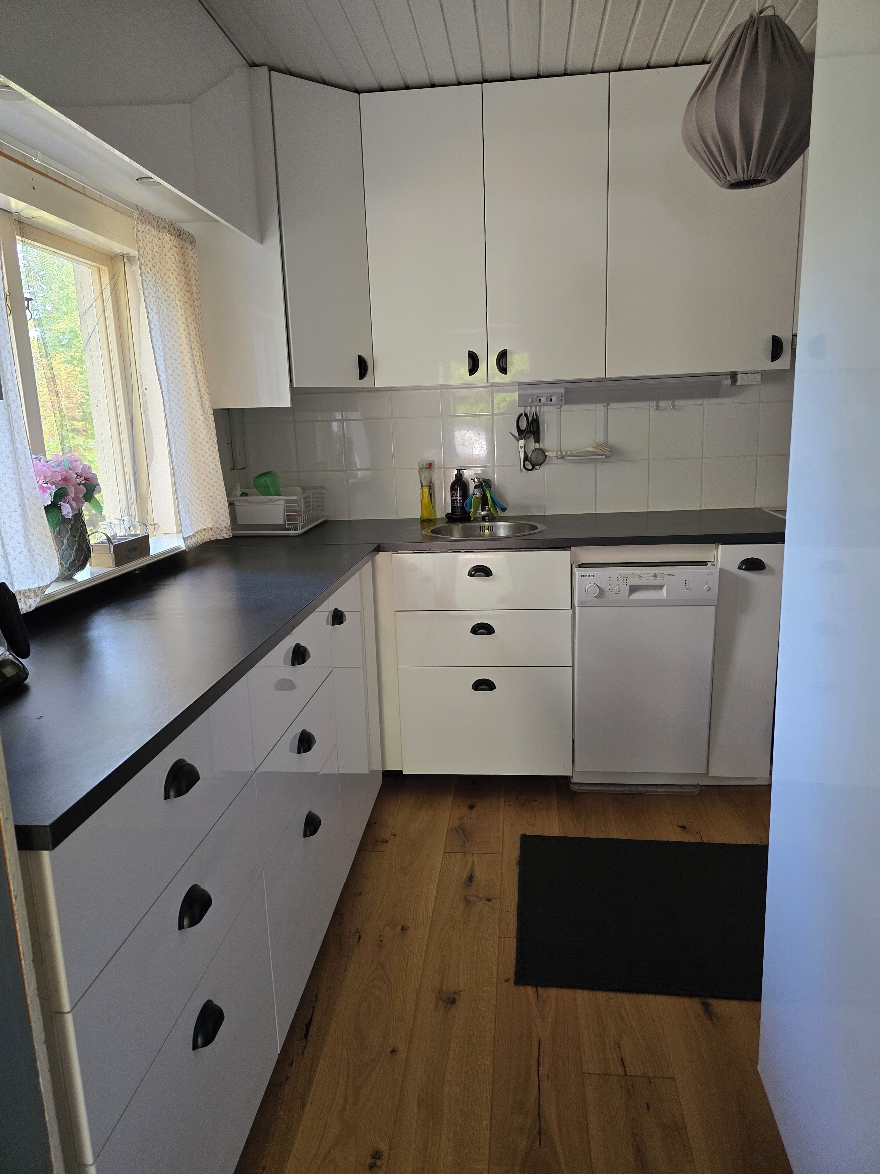A kitchen with white cabinets, a dishwasher, and a window with curtains.