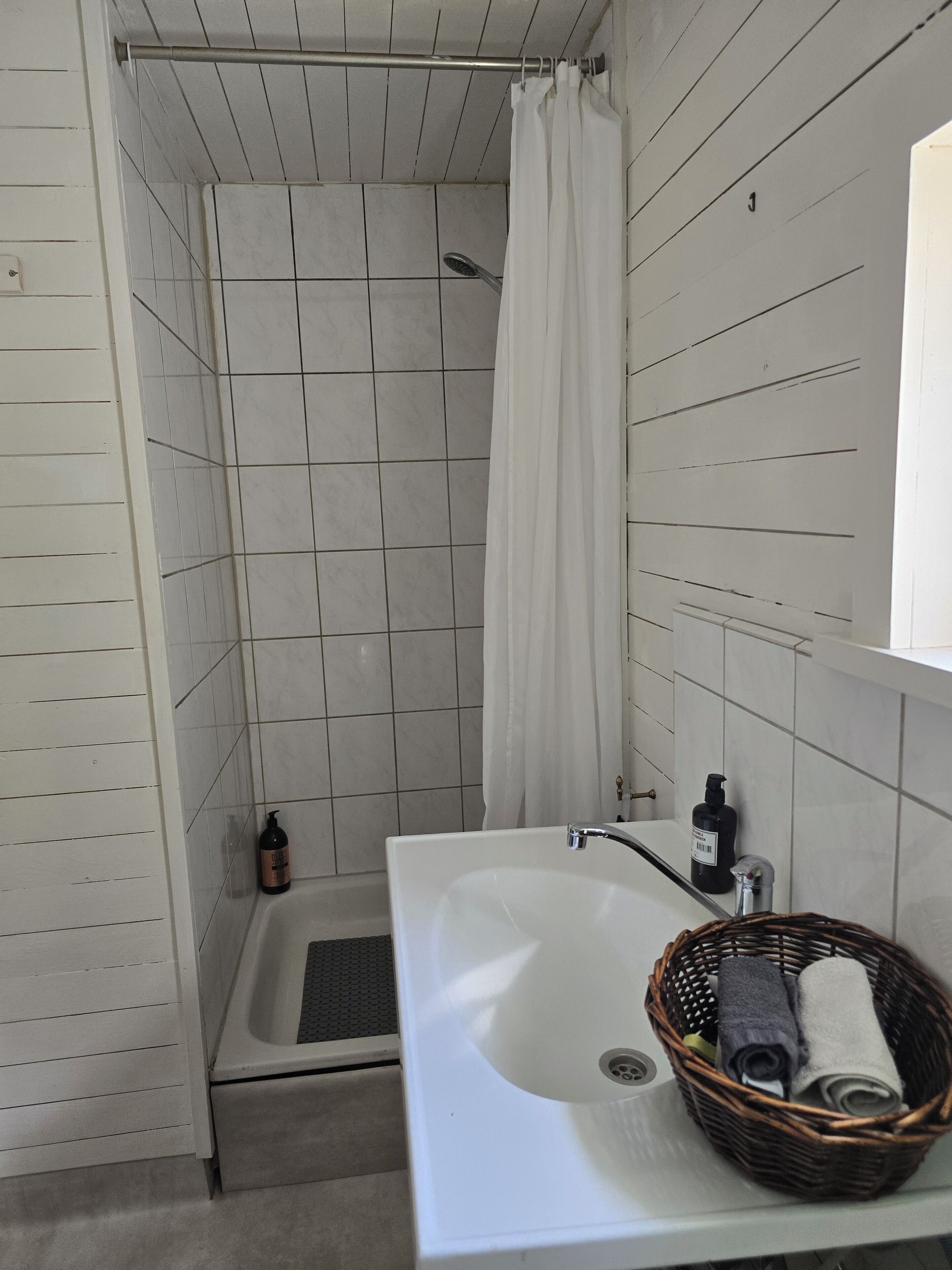 A bathroom with a shower, a sink, and a basket with towels.
