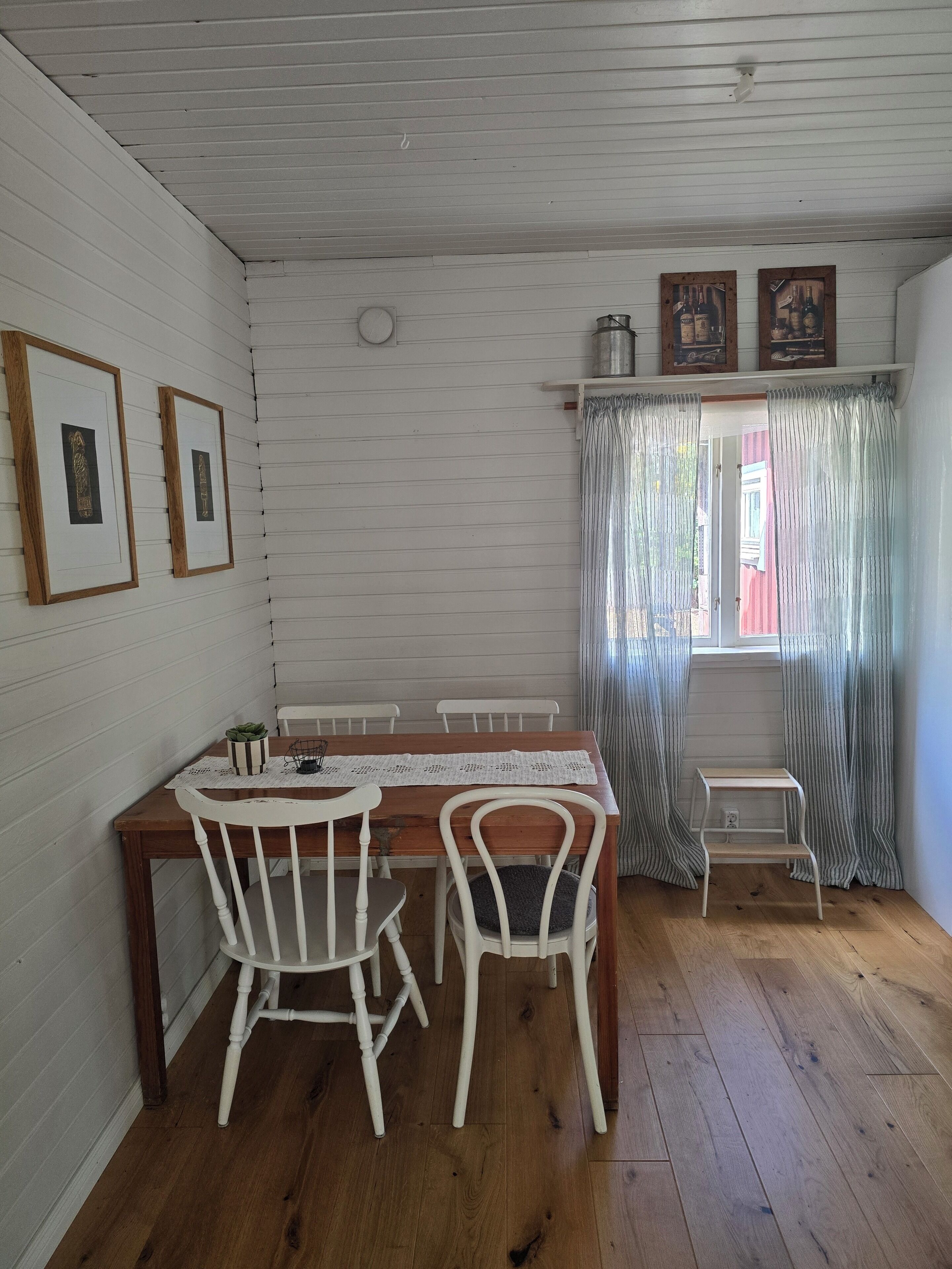 Un coin repas avec une table en bois, des chaises blanches et une petite étagère blanche.