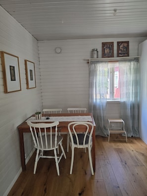 Un comedor con mesa de madera, sillas blancas y un pequeño estante blanco.