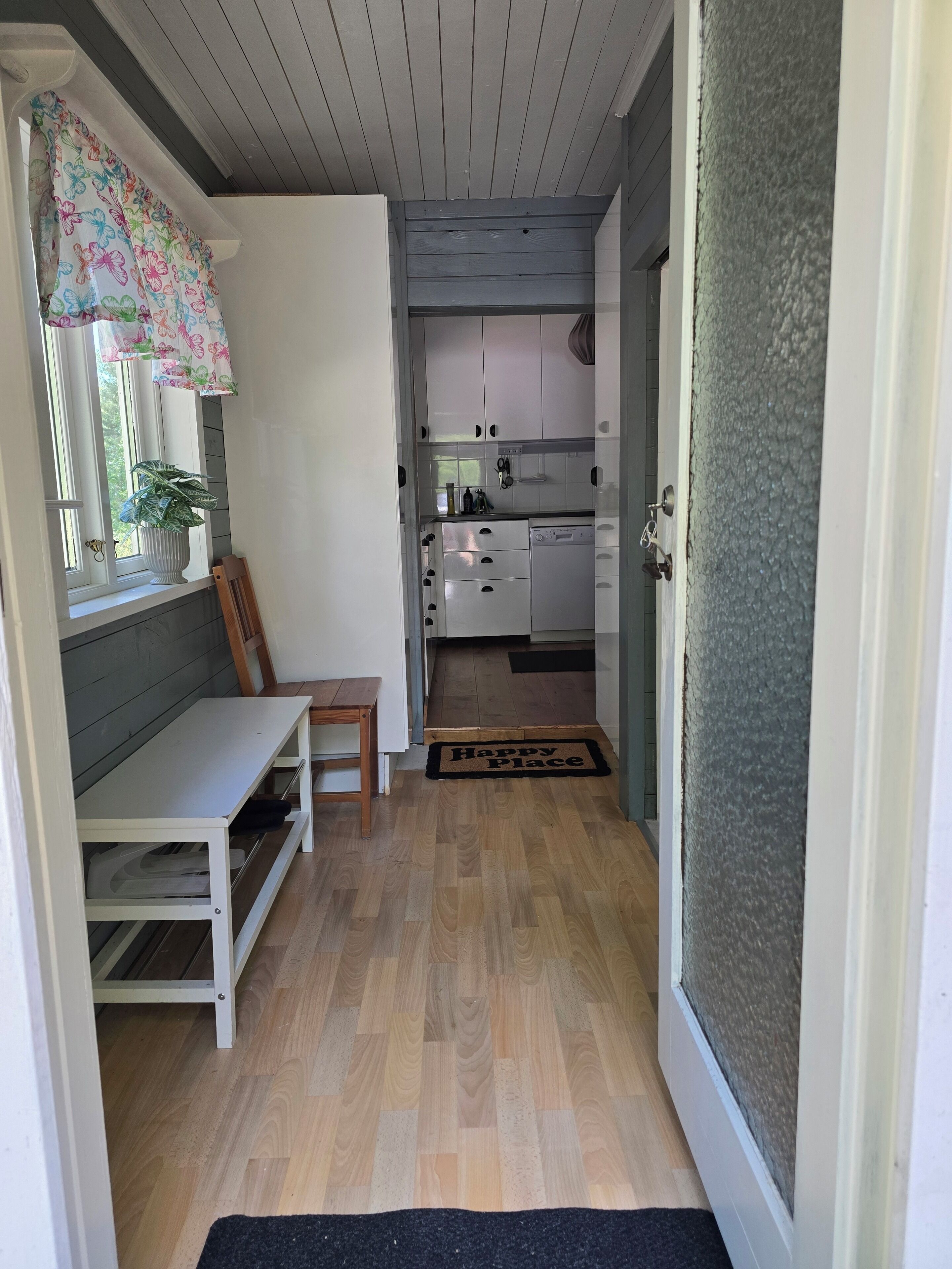 A compact kitchen with white cabinets, a wooden bench, and a potted plant.