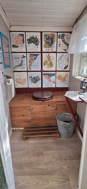 A compact room with a wooden floor, a small round table, a bucket, and a wall adorned with various country maps.