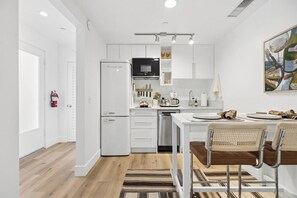 A modern kitchen with white cabinetry, a built-in oven, and a dining area with a table and chairs. - The Big Yellow House Loft C (Summerland)
