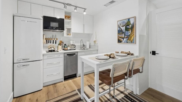 A compact kitchen with white cabinetry, a built-in microwave, and a dining area with a white table and two chairs. - The Big Yellow House Loft C (Summerland)