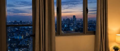 A hotel room with a city view, a bed, a nightstand, and curtains.
