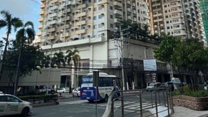 Um edifício residencial alto com várias varandas, um ponto de ônibus e uma rua com carros e um táxi.