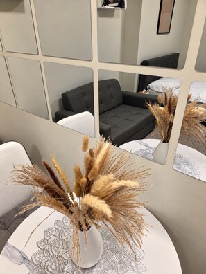 A room with a round table, a vase with dried plants, a grey sofa, and a mirror reflecting the room. - Le Petit Manhattan - 34th Floor Skyline Studio in Araneta City, Cubao (Quezon City)