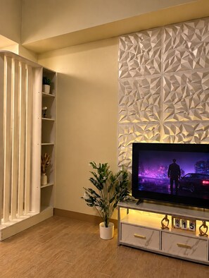 A modern living room with a flat-screen TV, a geometric wall panel, a white cabinet with gold handles, and a potted plant. - Le Petit Manhattan - 34th Floor Skyline Studio in Araneta City, Cubao (Quezon City)