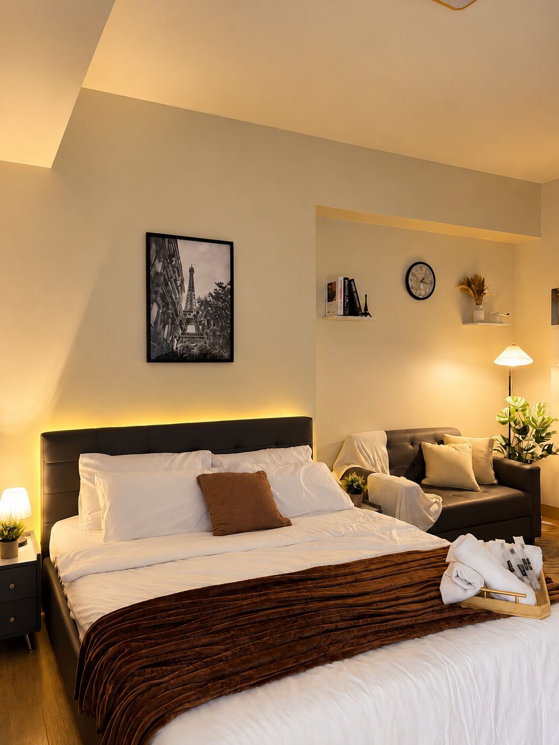 Une chambre d’hôtel avec un lit, des tables de chevet, un canapé, une horloge murale et un tableau encadré.