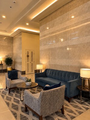 A modern lobby with a blue sofa, two armchairs, a coffee table, and a potted plant. - Le Petit Manhattan - 34th Floor Skyline Studio in Araneta City, Cubao (Quezon City)