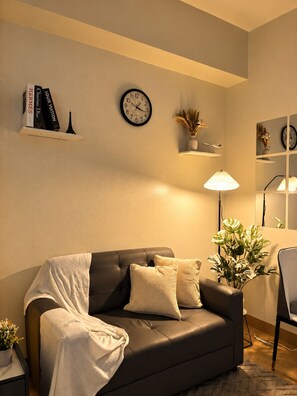 A living room with a sofa, a clock, a lamp, and a small plant. - Le Petit Manhattan - 34th Floor Skyline Studio in Araneta City, Cubao (Quezon City)