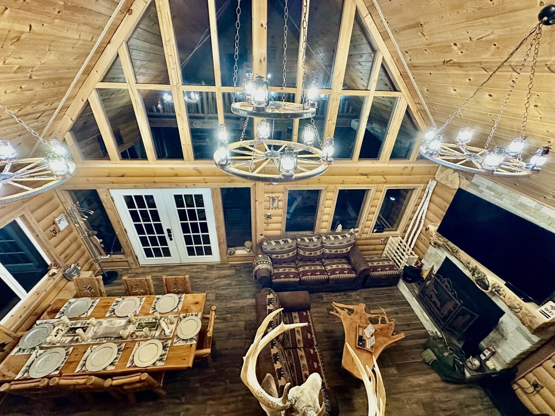 Um amplo quarto estilo loft com teto alto, vigas de madeira, uma grande mesa de jantar posta para seis pessoas, um sofá e uma lareira.