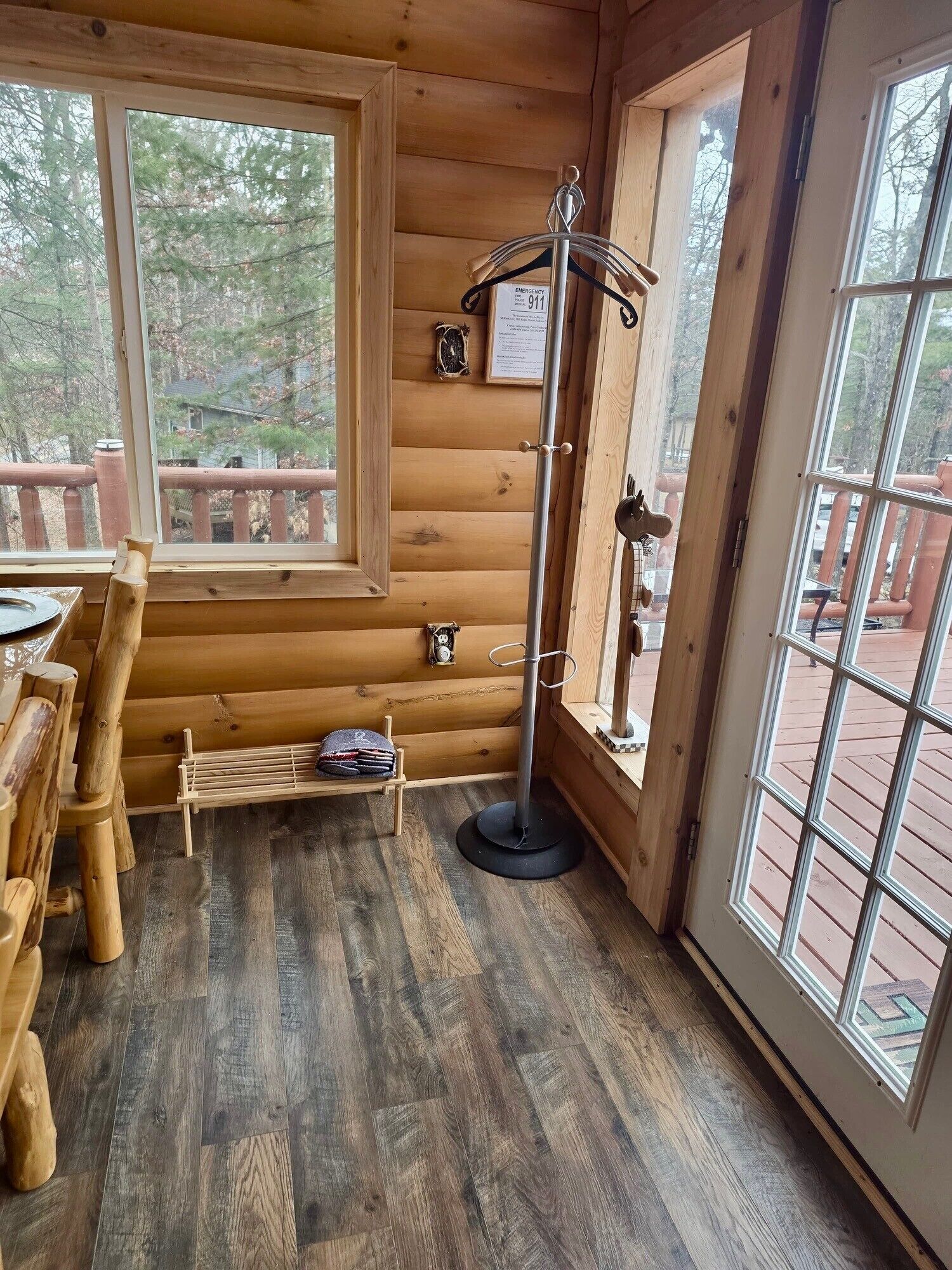 A wooden cabin interior with a dining table, chairs, a coat rack, and a window with a view of trees.