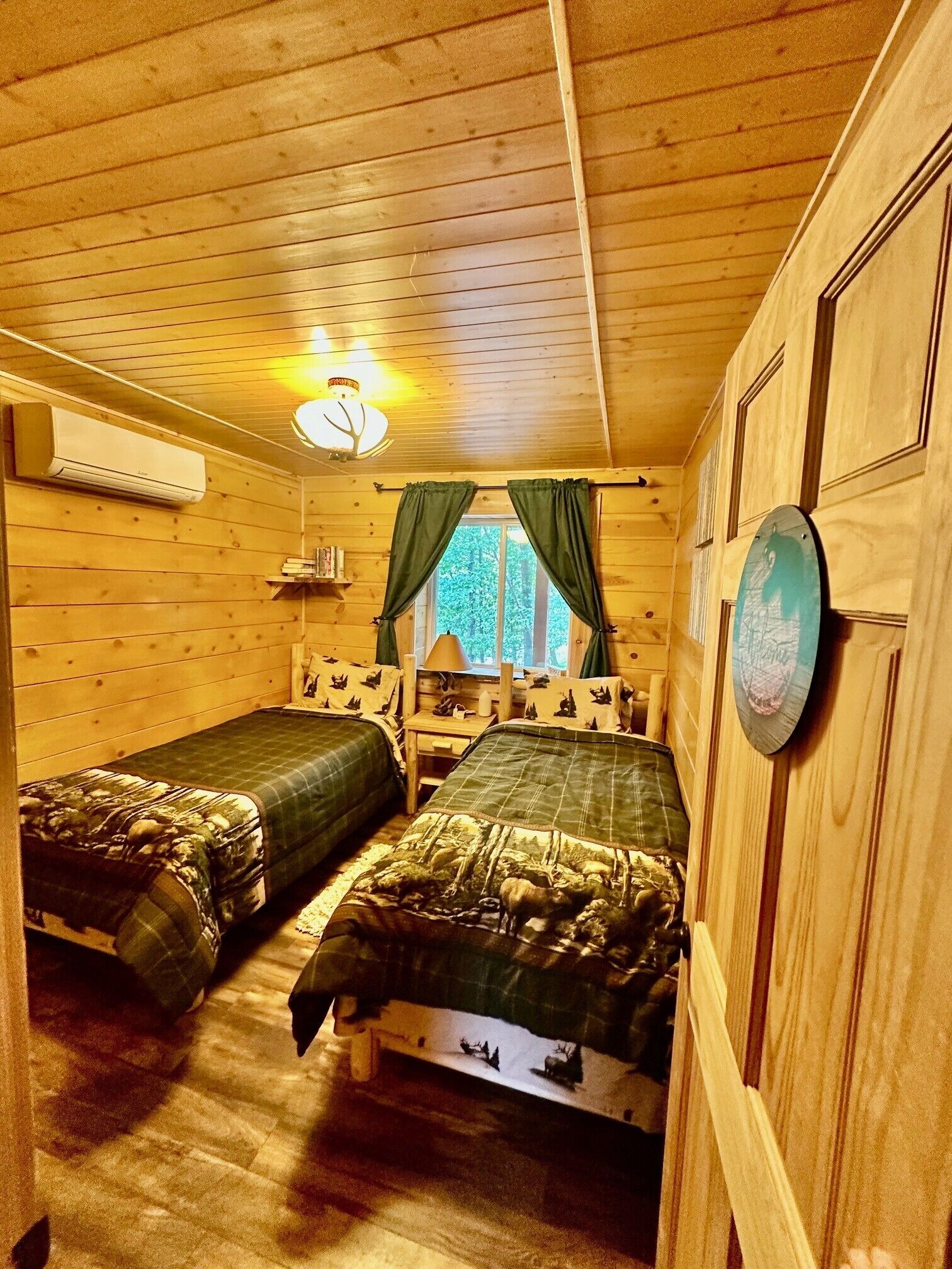 A cabin with two beds, a ceiling fan, a window with curtains, and a wall-mounted lamp.