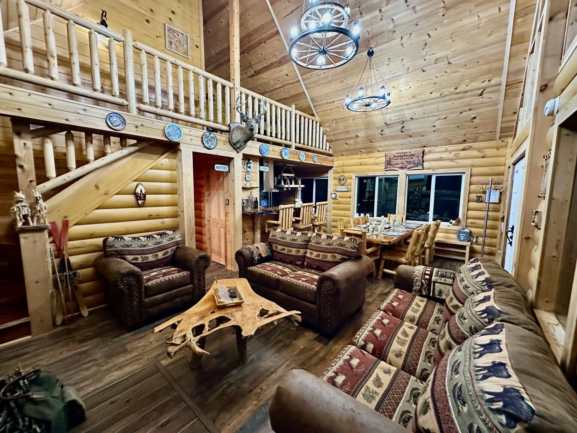 A log cabin interior with a dining area, a kitchen, and a staircase leading to an upper level.
